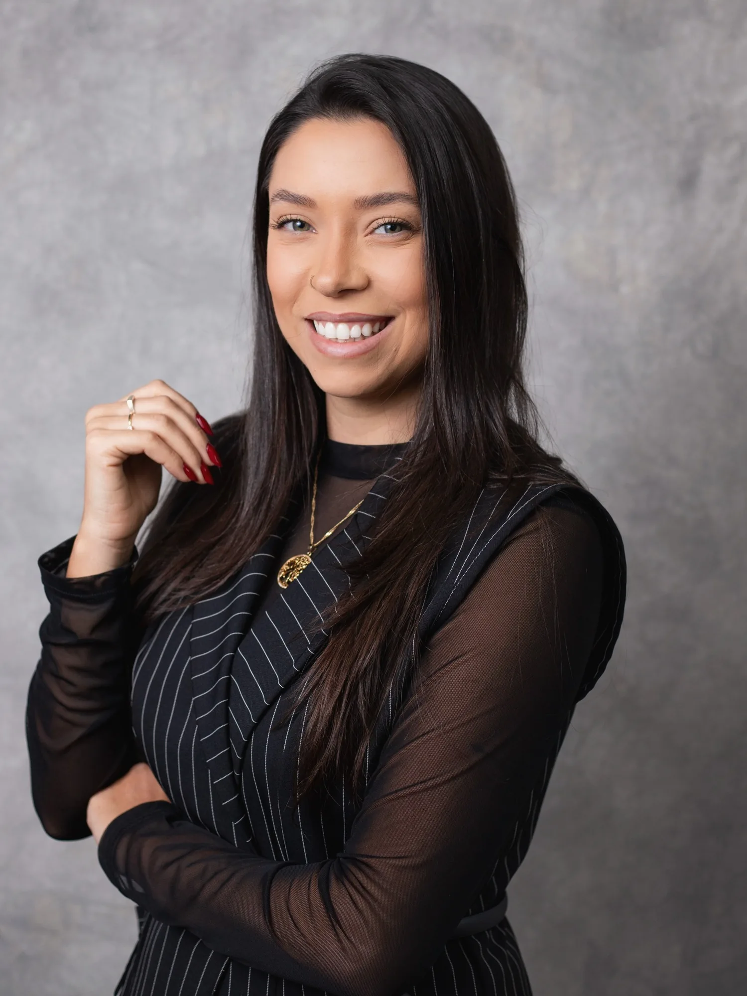 Amanda Siqueira, advogada, sorrindo, de colete listrado preto e colar dourado, sobre fundo cinza.